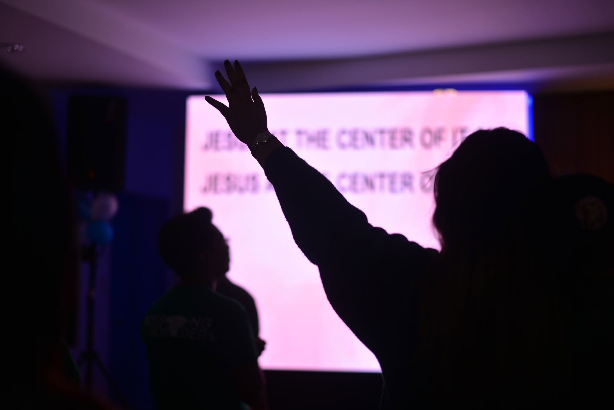 A person raising a hand in worship in front of a glowing lyrics screen